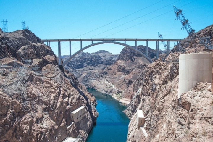 Bridge over a deep canyon with rocky walls and a river below on a sunny day.