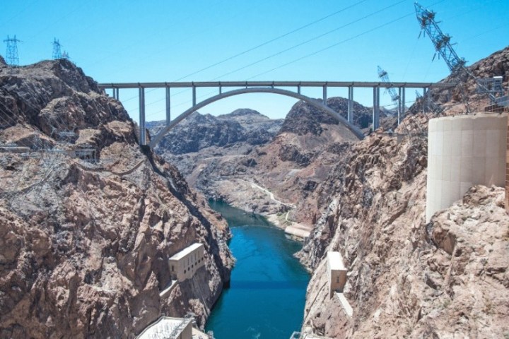 Bridge spans a rocky canyon over a blue river under a clear sky.