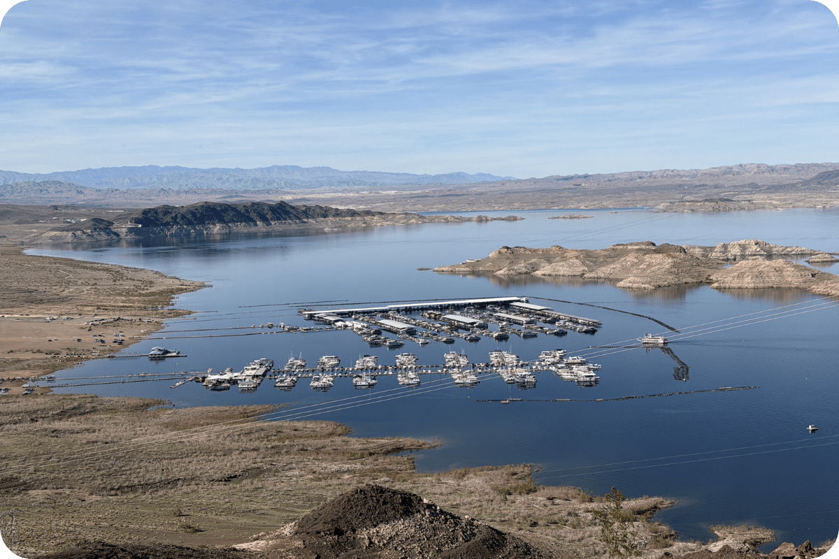Aerial view of a marina on a large body of water with distant hills and clear skies.